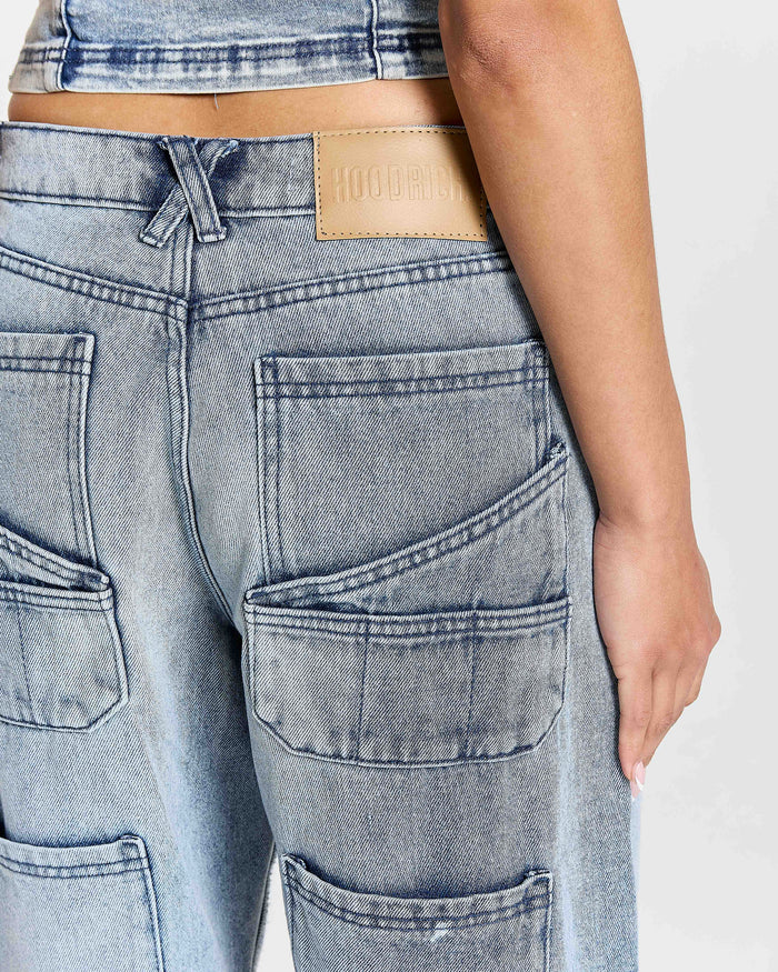 Close-up of a person wearing light blue jeans with a visible brand patch on a white background