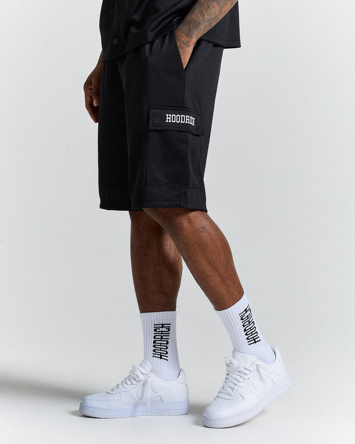 Person wearing black shorts with 'Hoodie' branding, white sneakers, and socks on a light gray background