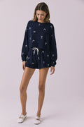 Full body view of woman wearing Chaser’s navy Tossed Bows Shorts with matching Tossed Bows Long Sleeve top on a white background