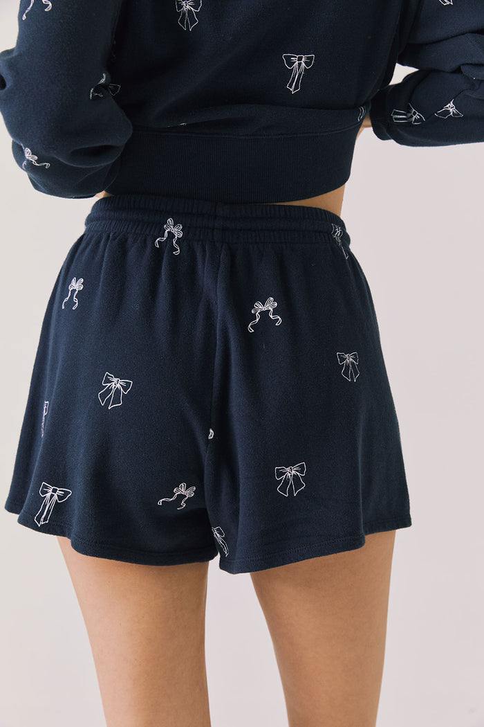 Back view of woman wearing Chaser’s navy Tossed Bows Shorts with allover bow pattern on a white background