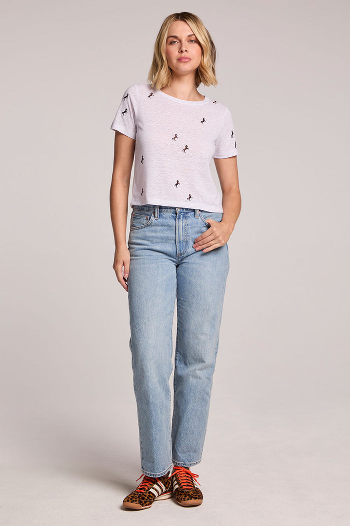 Front view of a woman wearing the Chaser  Tossed Horses Tee and sneakers on a neutral background