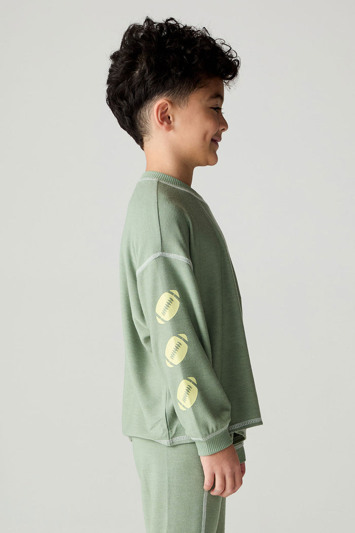 Side view of a boy wearing the Chaser Touchdown Boys Tee on a neutral background with long-sleeve shirt