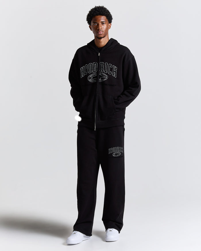 Person wearing a black hoodie and pants with 'Hoodrich' branding on a light gray background