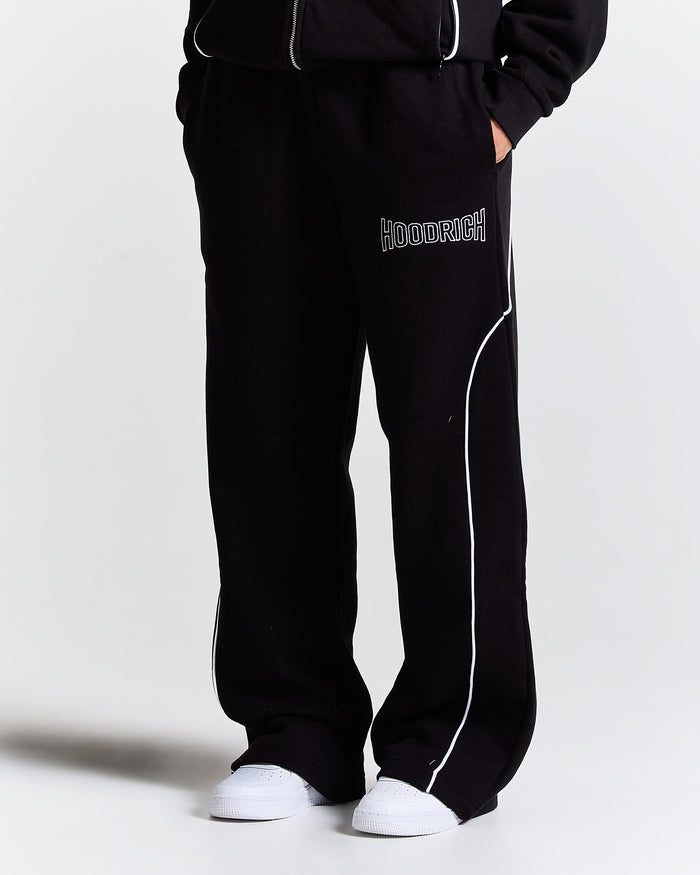 Model wearing oversized black joggers with white piping detail and Hoodrich logo embroidery.