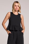 Front view of a woman wearing a black Chaser Liberty tank set with her hands in her pockets on a neutral background