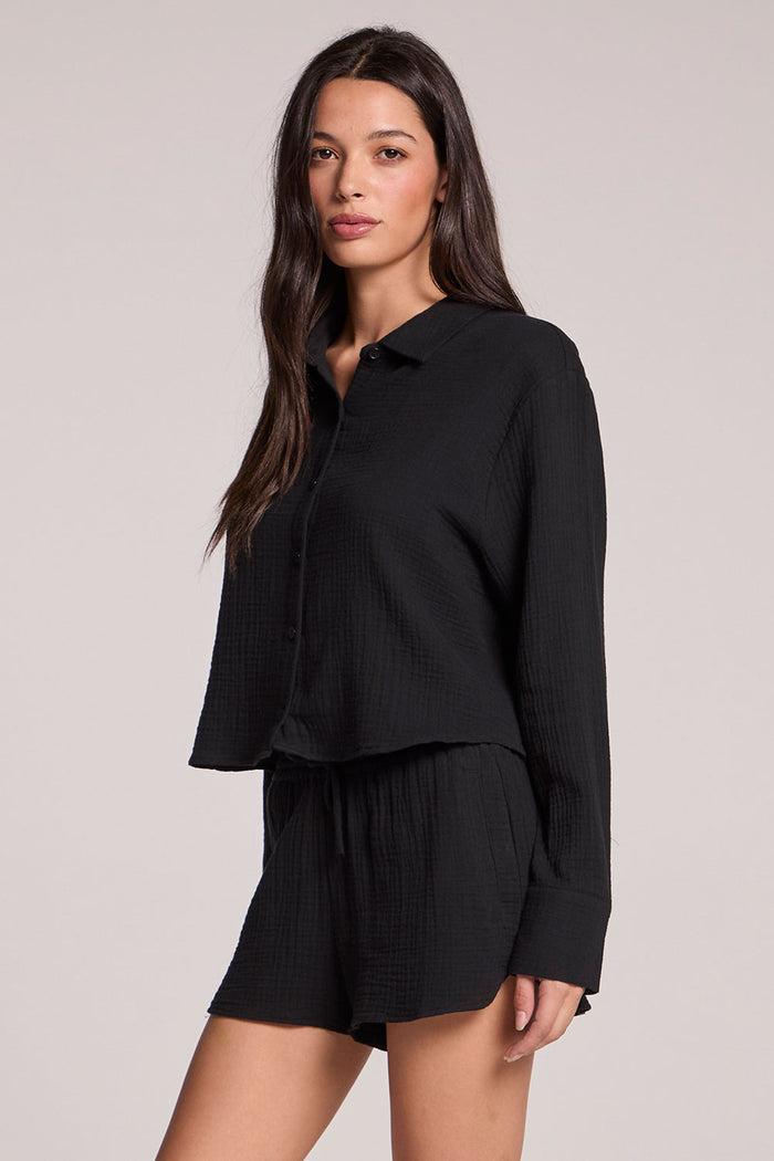 Side angle view of a woman wearing the Chaser Paso long sleeve with matching shorts in true black on a neutral background