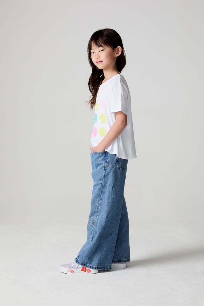 Full body side view of a girl wearing the Chaser Unicorn Parade Tee on a neutral background