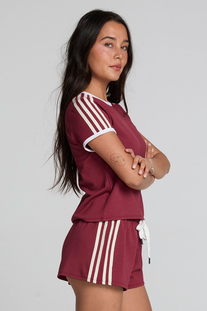 Side view of a woman wearing the Chaser Urban Burnt Red Tee on a neutral background with red shorts