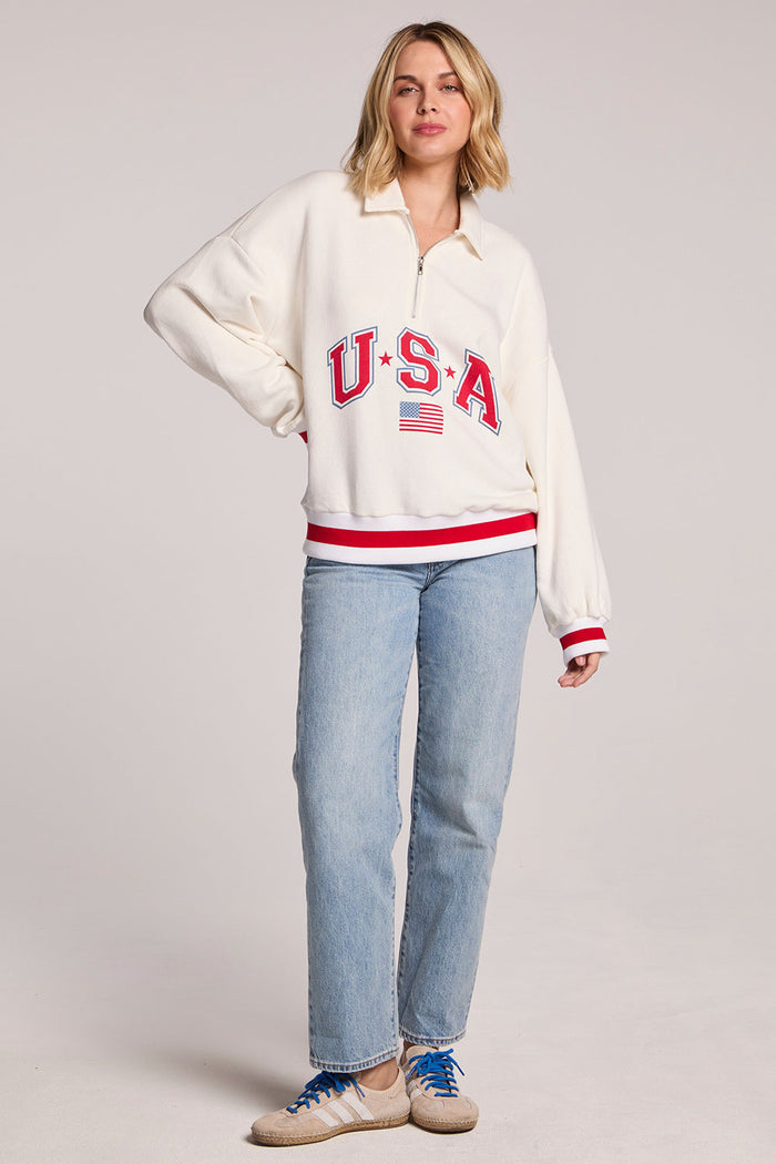 Full body ront view of a woman wearing the Chaser USA Pullover and jeans with one hand on her hip on a neutral background