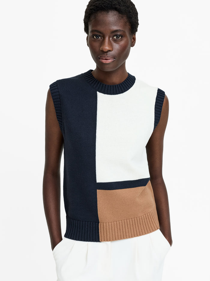 A woman wearing a sleeveless navy, white and beige colour block knit vest with a round ribbed neckline and hem.