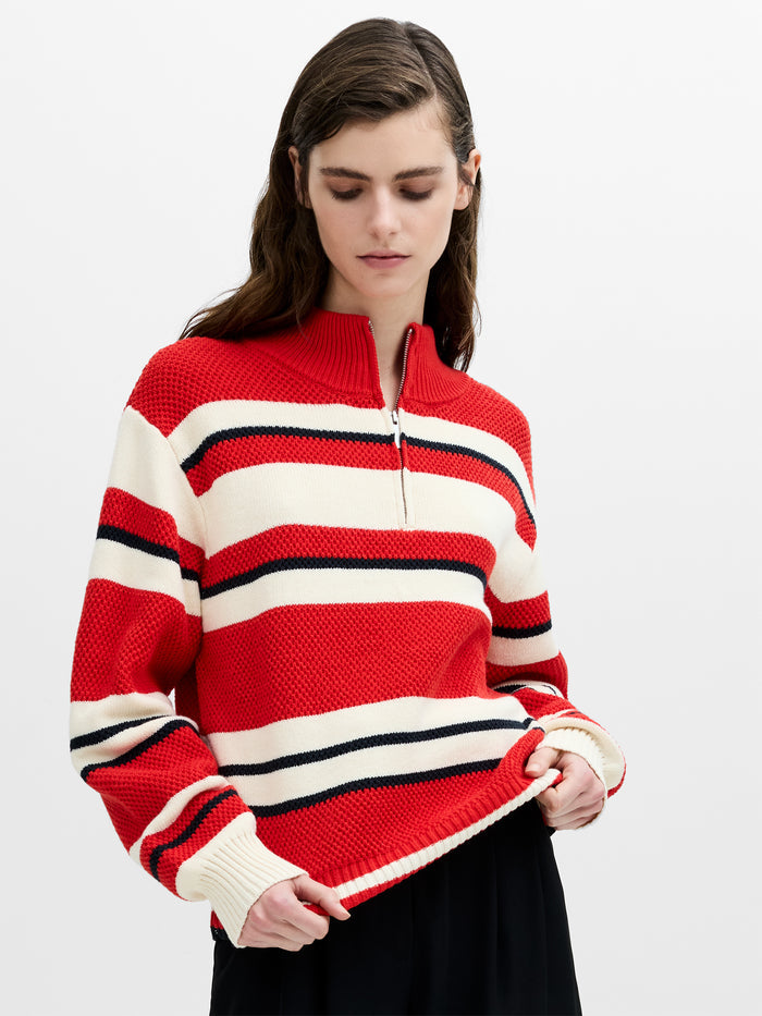 A woman wearing a red, white and black striped half zip jumper with long balloon sleeves and dropped shoulders.