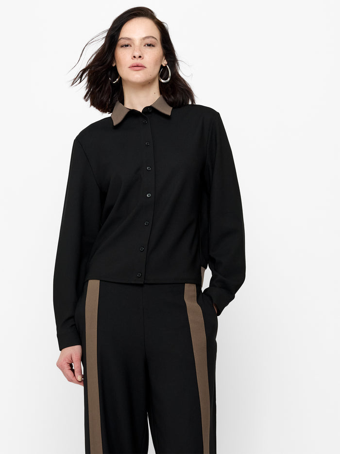 A woman wearing a black and brown Shirt with drop shoulders, long sleeves, a collared neckline and a button down fastening.