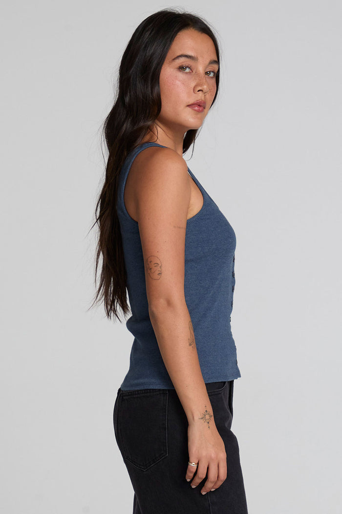 Side view of a woman wearing the Chaser Velora Dark Denim Tank on a neutral background with hands lowered
