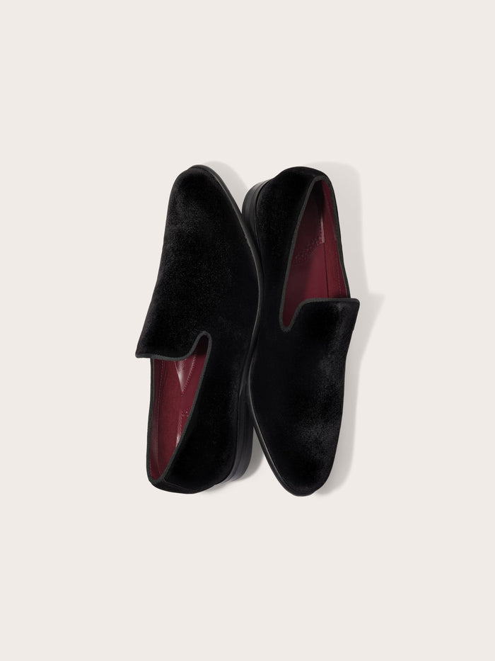 Pair of black velvet slip-on shoes with burgundy lining, top view on cream background