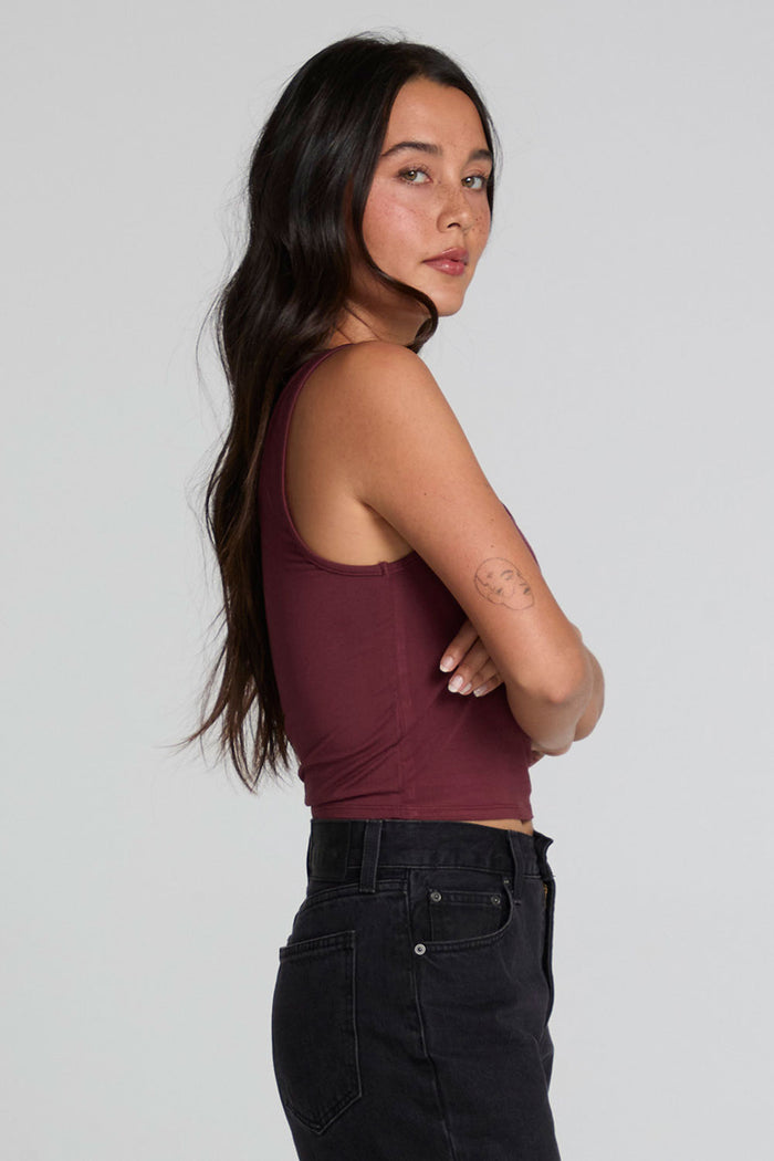 Side view of a woman wearing the Chaser Verze Brick Tank and jeans on a neutral background with arms crossed