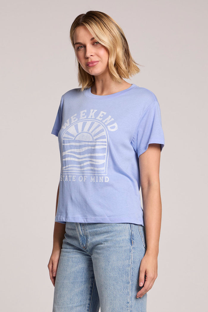 Side angle view of a woman wearing the Chaser  Weekend State Of Mind Tee on a neutral background with her arms at her sides