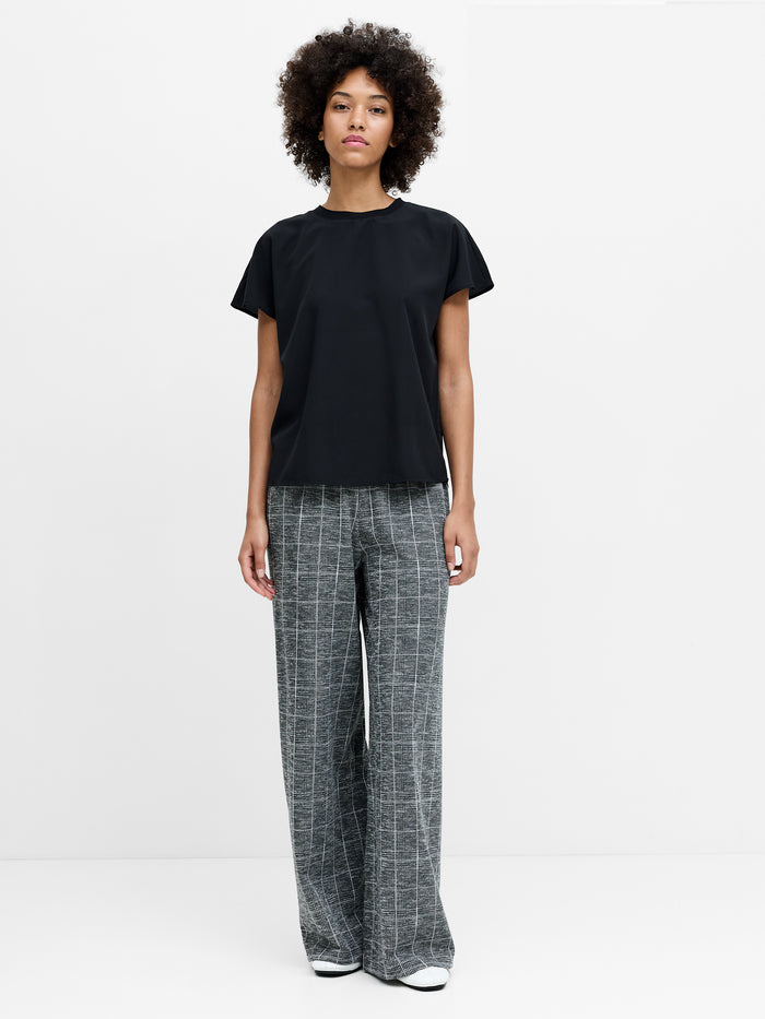 A woman wearing grey full length, wide leg trousers with an elasticated waistband and a subtle checked pattern.