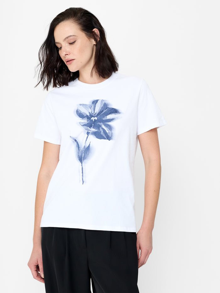 A woman wearing a soft cotton white T-shirt with a blurred graphic flower, a crew neck and short sleeves.