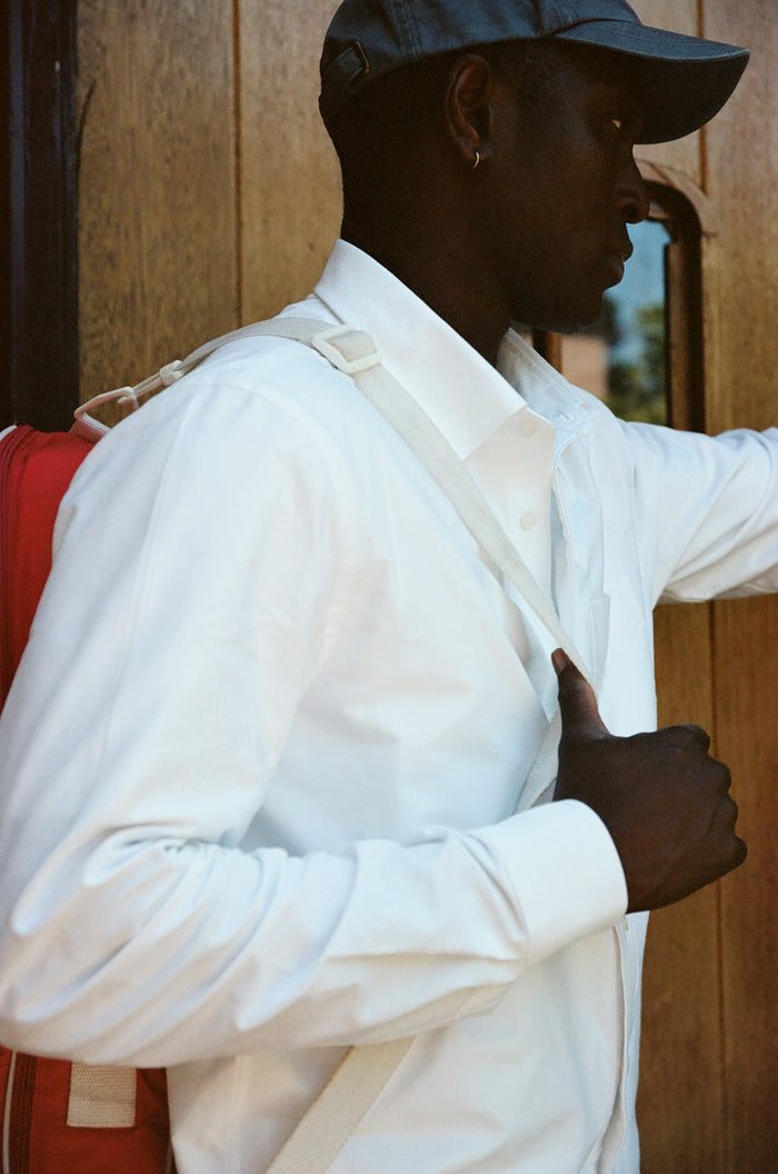 Man in white oxford shirt with bag strap, side profile outdoors