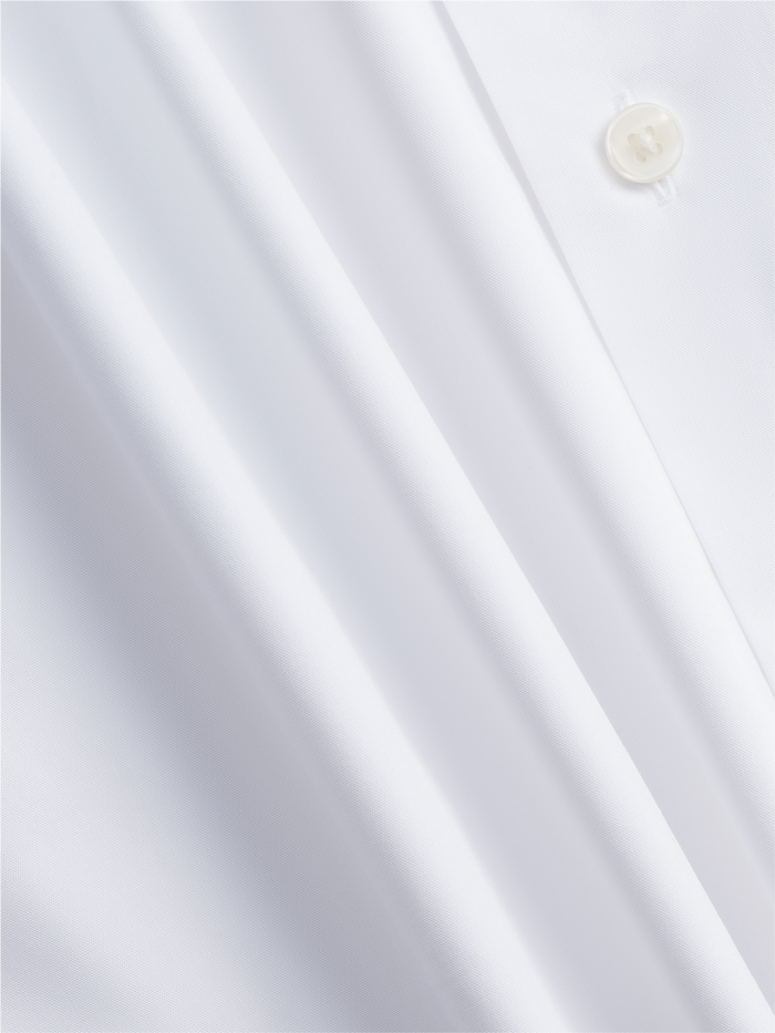 Close-up of white oxford shirt fabric with button and soft folds