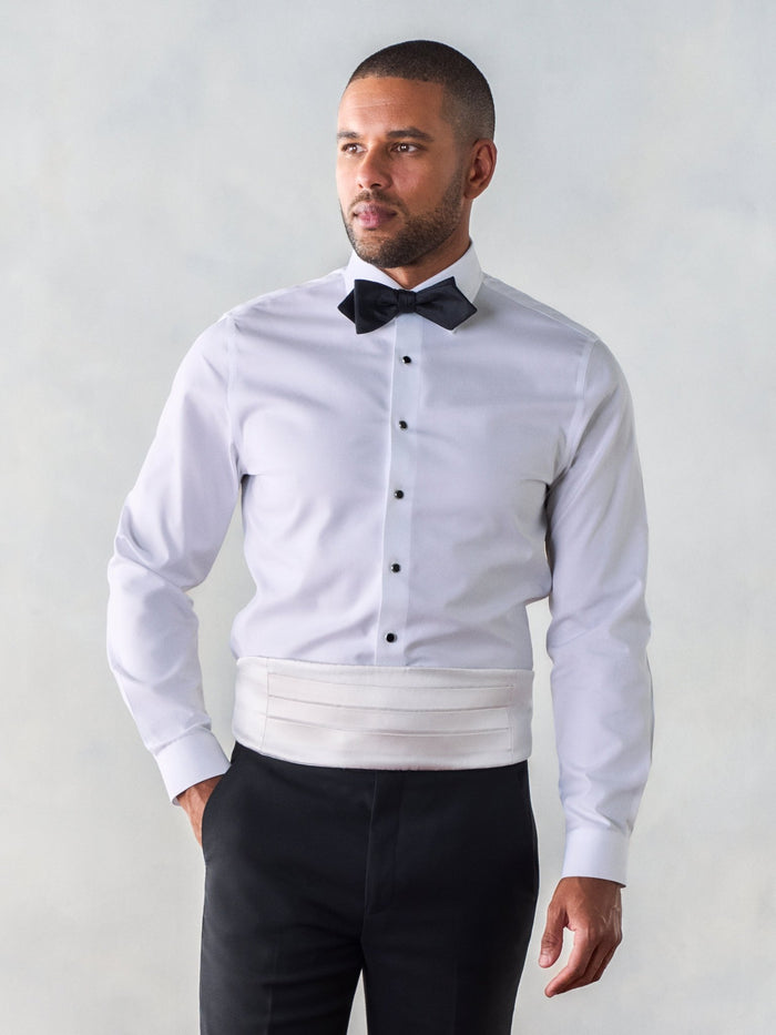Man in a white tuxedo shirt with a white satin cummerbund and black bow tie.