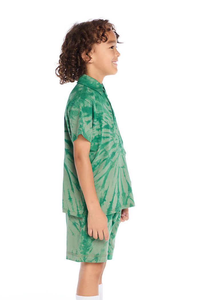 Side view of boy wearing the Chaser Kids Wild Green Tie Dye Polo Shirt showing short sleeves and relaxed fit, styled with matching tie dye shorts and silver sneakers on a white background