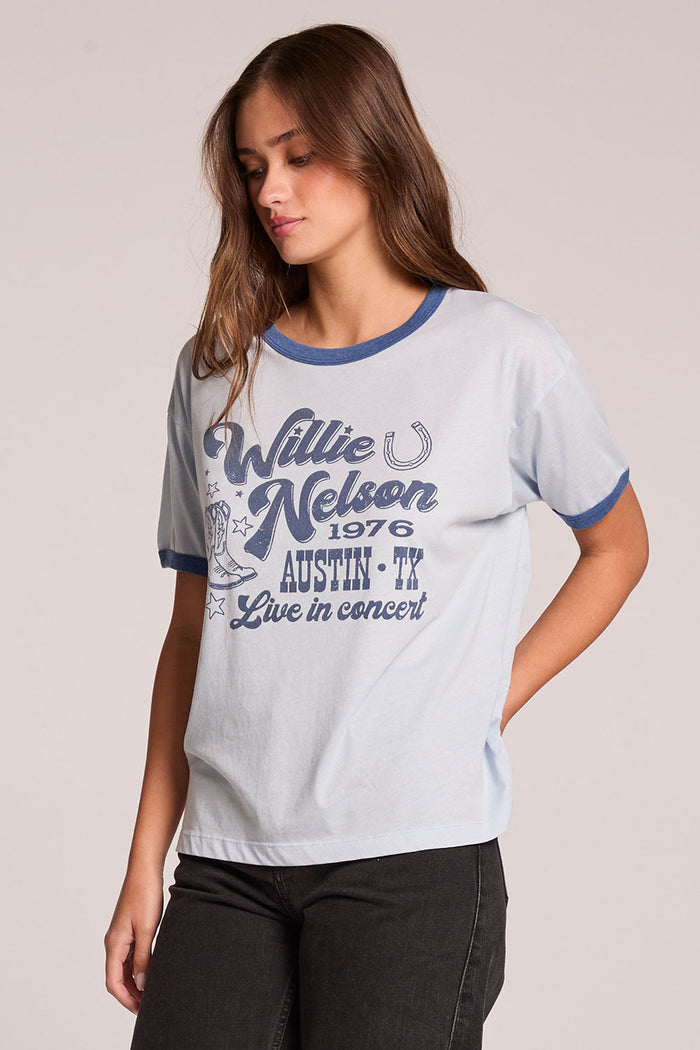 Side angle view of a woman wearing the Chaser  Willie Nelson Austin 1976 on a neutral background with one hand on her hip