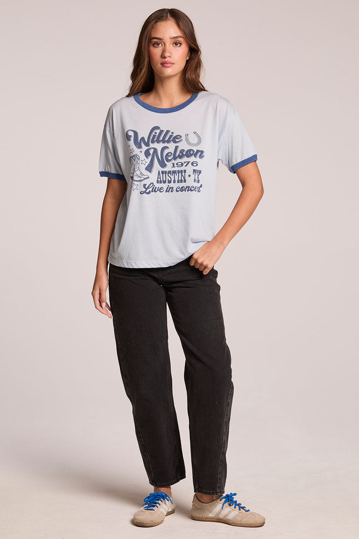 Full body front view of a woman wearing the Chaser Willie Nelson Austin 1976  with hands in her pockets on a neutral background