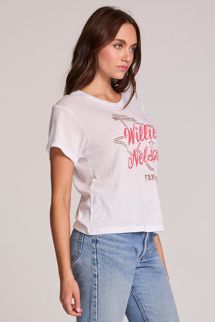 Side view of a woman wearing the Chaser Willie Nelson Fan Club Tee on a neutral background with arms at sides and jeans