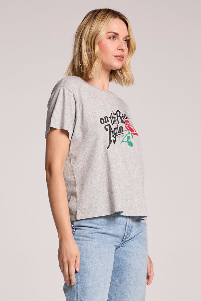 Side angle view of a woman wearing the Chaser Willie Nelson On The Road Again Tee and jeans on a neutral background