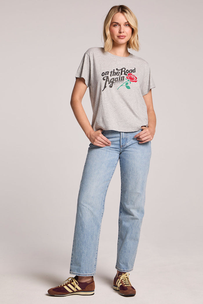 Full on front view of a woman wearing the Chaser Willie Nelson On The Road Again Tee and sneakers on a neutral background