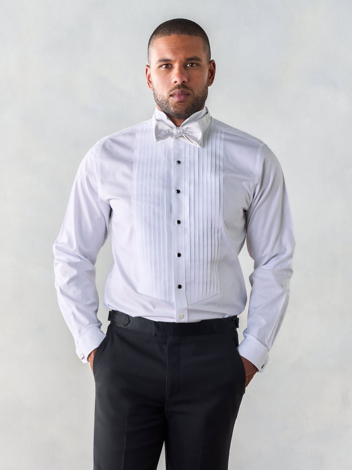 Man in white wing-tip tuxedo shirt with pleated bib, white bow tie and black studs, front view