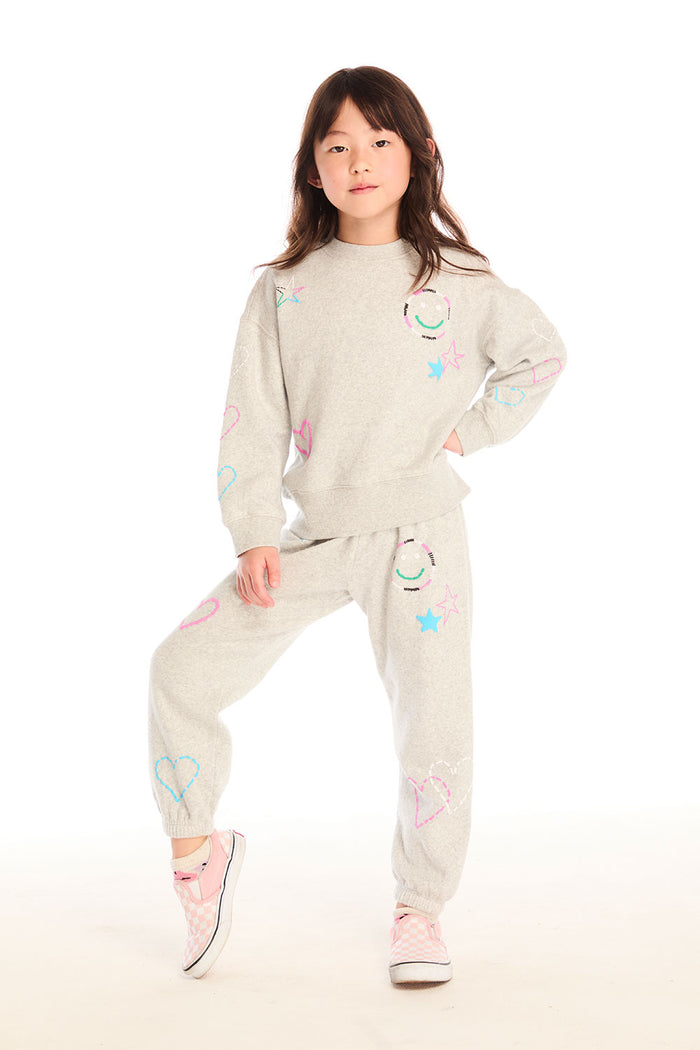 Full body view of girl wearing Chaser’s light gray Winter Love Pants and matching Winter Love Stitches Long Sleeve with colorful designs on a white background