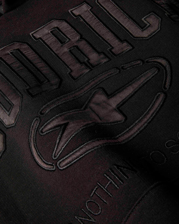 Close-up of a dark embroidered graphic on fabric, showing large raised letters and a stylized logo in a very dark brown or charcoal tone against a black background.