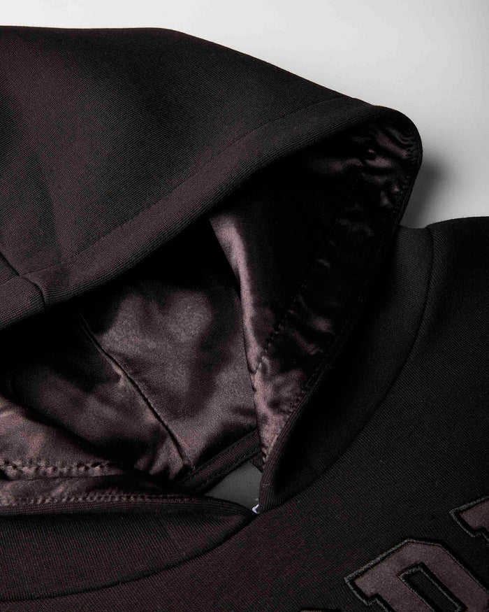 Close-up of a black hooded sweatshirt showing the interior lining of the hood and shoulder area against a light gray background.