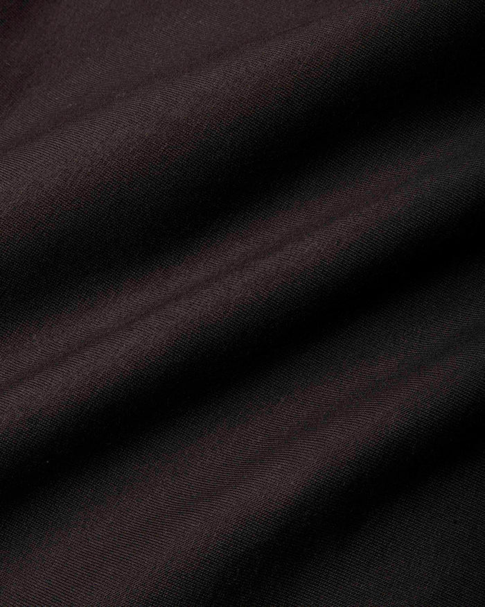 A close-up of dark, draped fabric with a fine ribbed texture, showing soft folds and shadows.