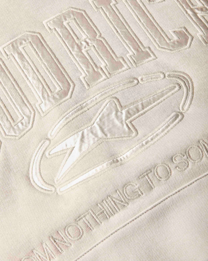 Close-up of a cream-colored fabric surface with tonal, raised embroidered lettering and a lightning bolt graphic.