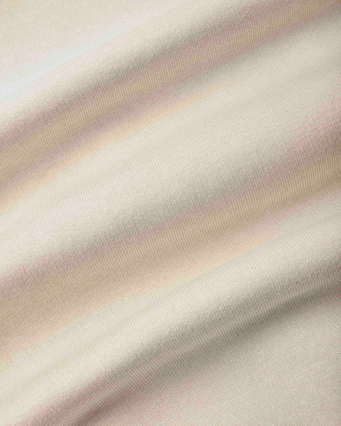 A close-up of draped fabric with a soft, warm off-white or cream tone and subtle pinkish-beige shading from the folds.