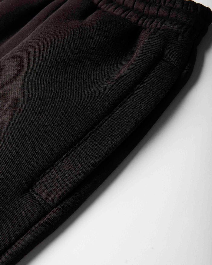Close-up of black sweatpants showing the elastic waistband and side seam details against a light gray background.