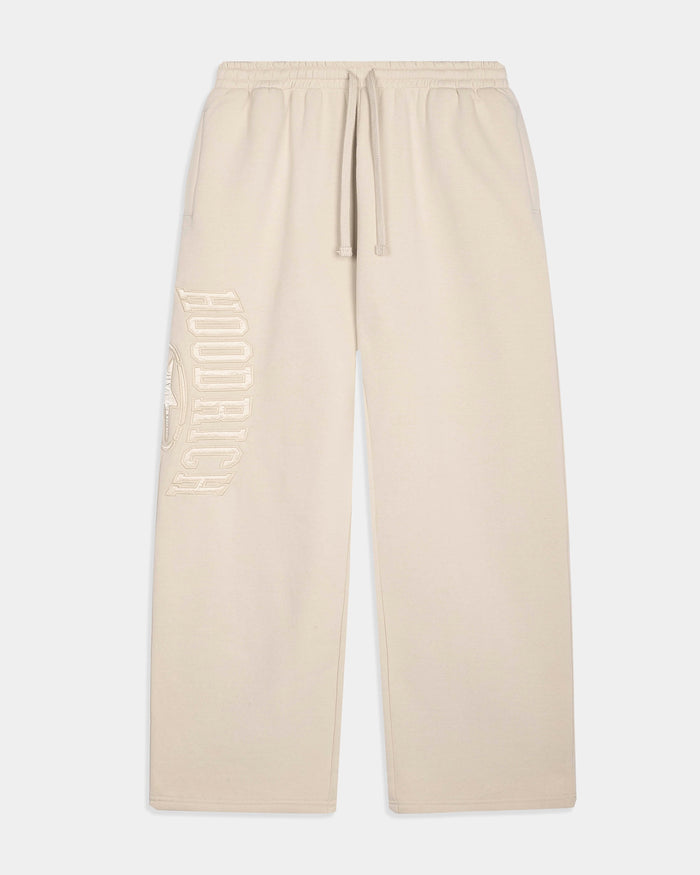 Cream-colored sweatpants with a drawstring waist and a tonal vertical 'HOODRICH' logo printed on the left leg, shown against a light gray background.