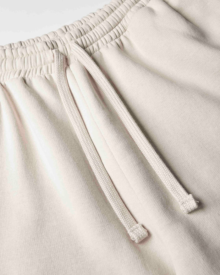 Close-up of a pair of light beige or cream-colored sweatpants, showing the elastic waistband and matching drawstring.