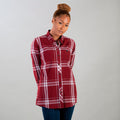 A woman with curly hair in a bun wears the Women's Breeze Shirt- Merlot Red, paired with dark jeans, standing against a plain light gray background with her hands behind her back.