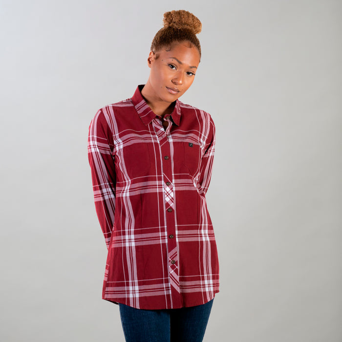 A woman with curly hair in a bun wears the Women's Breeze Shirt- Merlot Red, paired with dark jeans, standing against a plain light gray background with her hands behind her back.