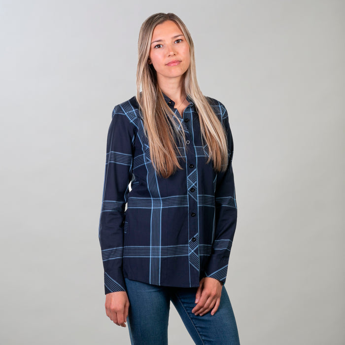 A woman with long blonde hair poses against a light gray background, wearing the Women's Breeze Shirt in Ocean Blue and blue jeans. She looks at the camera with a neutral expression.