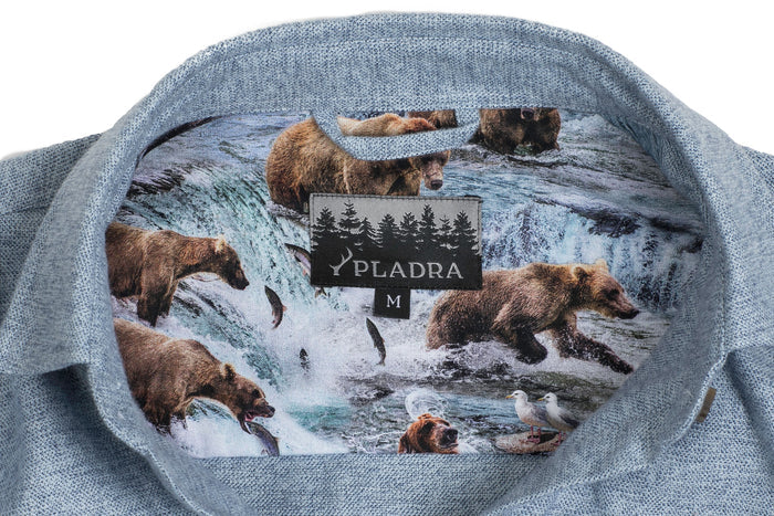 The Women's Cascade Flannel Shirt in Dusty Blue features a turned-out collar revealing a vibrant bear-and-fish inner lining, a Pladra label, and size M tag—crafted from heavy brushed cotton in the iconic Cascade style.