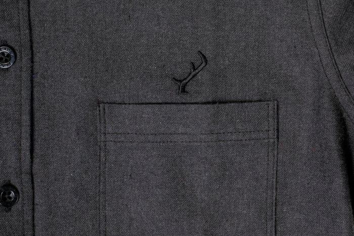 Close-up of the Women's Cascade Flannel Shirt in Jet Black Heather, featuring heathered cotton and a chest pocket with an embroidered black antler above it. Two black buttons are partially visible on the left side.