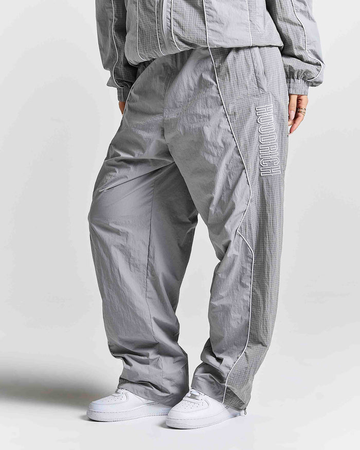A person wearing loose-fit gray pants with a subtle grid texture, white sneakers, and a matching gray jacket against a light gray studio background.
