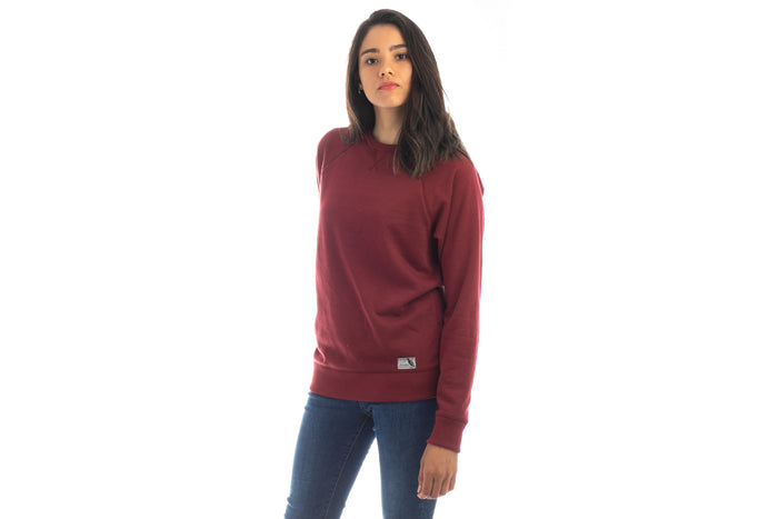 Woman wears a Pladra Women's Crew Neck Sweatshirt in Pomegranate Red and blue jeans, standing against a white background.