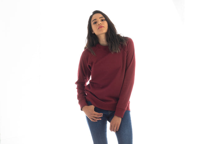 A woman with long dark hair wears a Pladra Women's Crew Neck Sweatshirt in Pomegranate Red and blue jeans.