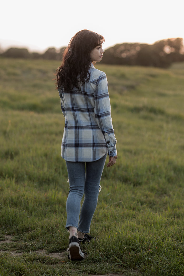 Woman with long dark hair walks in a grassy field at sunset, wearing a Pladra Women's Every Day Double Weave Shirt-Birch White.